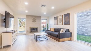 Una sala de estar moderna con sofá, mesa de centro, televisor, chimenea y ventanas amplias.