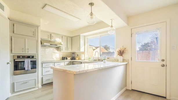 Una cocina moderna con una isla central, horno integrado e iluminación colgante.