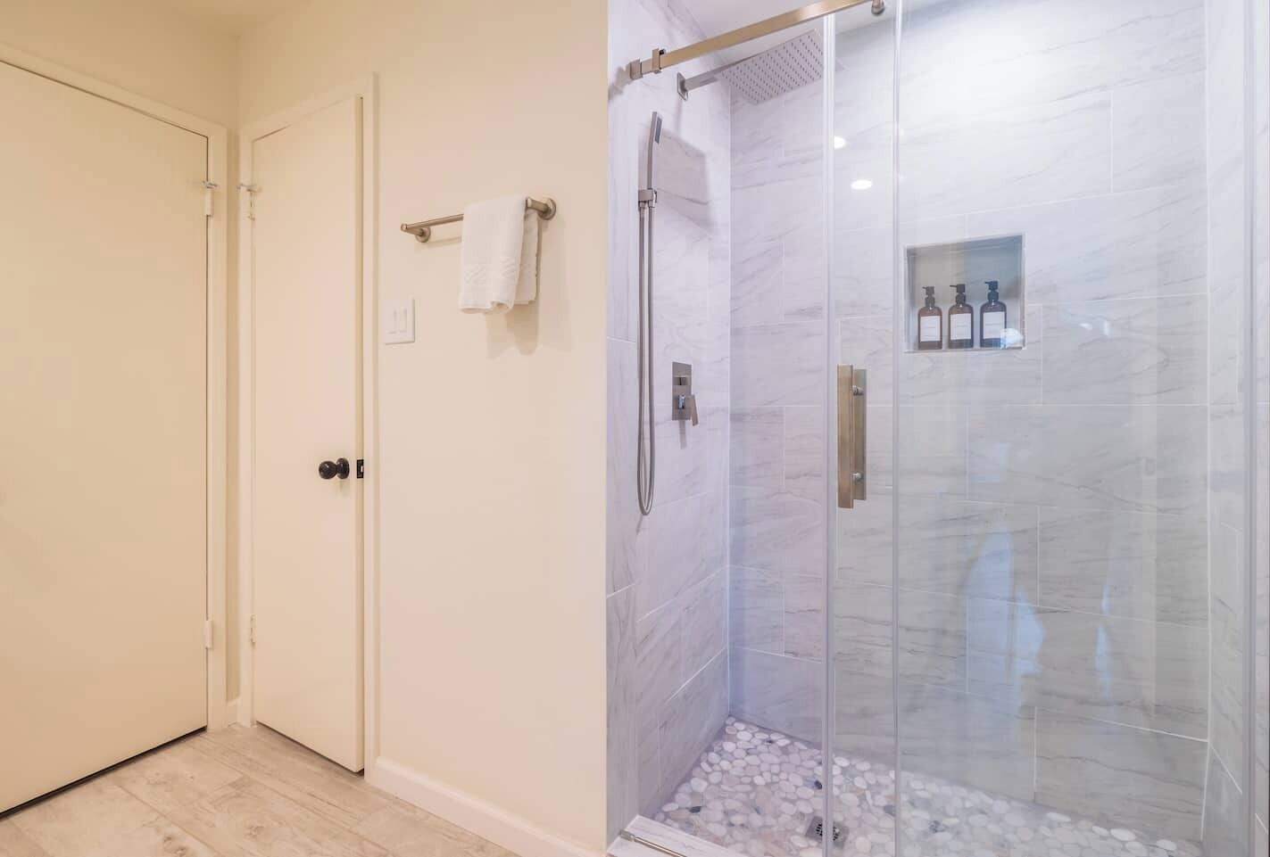 Et badeværelse med glasvægs brusebad, et håndklædestativ og en lille hylde med toiletartikler.