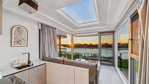 A balcony with a view of a lake, a sofa, a small table, and a kitchen area with a sink and cabinets. - One-of-a-kind tiny home designed for an unforgettable stay by the beautiful San Jacinto River (Highlands)