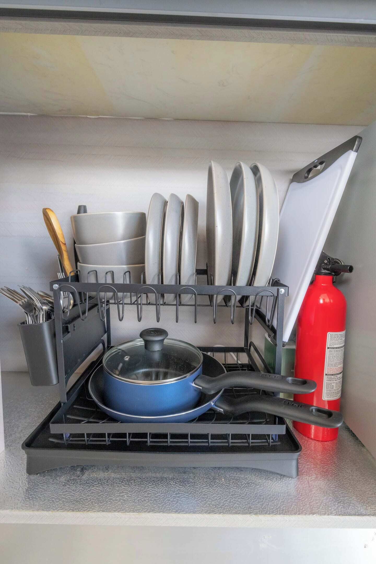 A kitchen with a dish rack, utensils, a blue pan, and a red fire extinguisher.