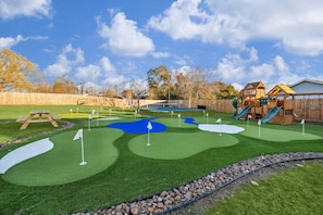Un parcours de mini-golf avec gazon synthétique, des bunkers de sable et une maison de jeu en bois.
