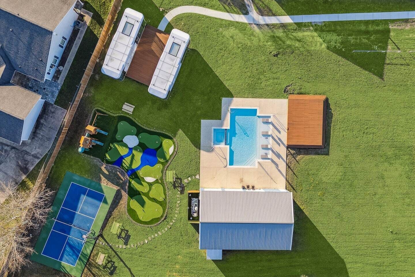 An aerial view of a property with a swimming pool, tennis court, and a building with a sloped roof.
