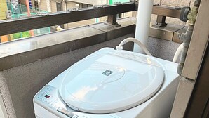 En tvättmaskin med frontmatning och en kontrollpanel, placerad på ett betonggolv intill ett fönster.