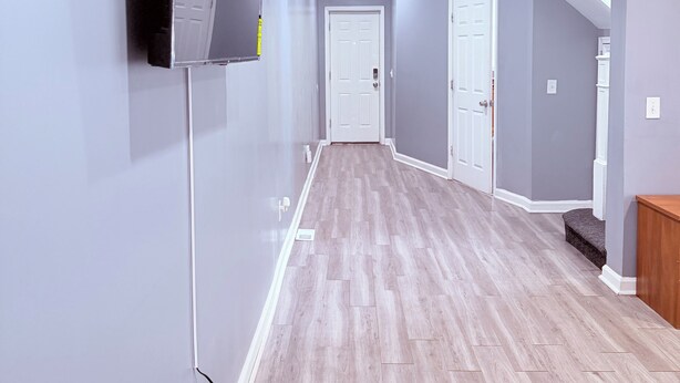 A hallway with a flat-screen TV mounted on the wall, a wooden floor, and a white door at the end. - Lovely 4 Bedrooms Family home, 20 minutes from Downtown. (Baltimore)