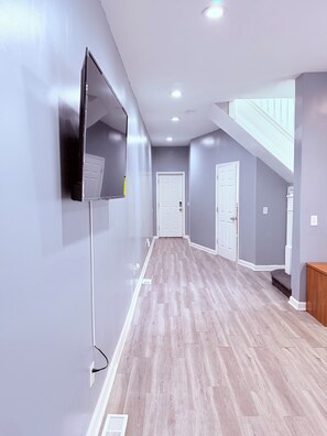 Ein Flur mit an der Wand befestigtem Flachbildfernseher, Holzboden und einer weißen Tür am Ende.