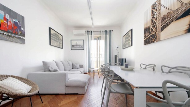A modern living room with a sofa, dining table, chairs, and artwork on the walls. - Albertelli - Large and comfortable apartment for 6 (Roma)