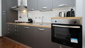 A modern kitchen with grey cabinets, a stainless steel range hood, a built-in oven, and a coffee maker. - Albertelli - Large and comfortable apartment for 6 (Roma)