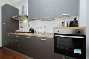 A modern kitchen with grey cabinets, a stainless steel range hood, a built-in oven, and a coffee maker. - Albertelli - Large and comfortable apartment for 6 (Roma)