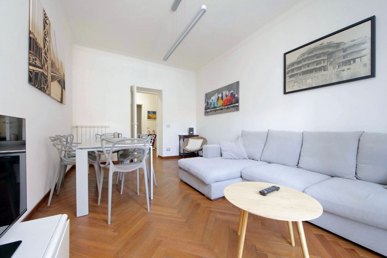 Una sala de estar moderna con un sofá gris, una mesa de comedor con sillas, una pequeña mesa redonda de centro y un televisor.