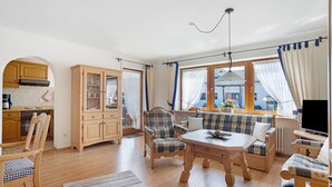 A cozy living room with a sofa, chairs, a table, and a kitchen area with cabinets and a stove. - Apartment 'Haus Grüntensee' with Balcony and Wi-Fi (Wertach)