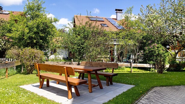 A picnic table with benches in a grassy area, surrounded by trees and a building with a tiled roof. - Apartment 'Haus Grüntensee' with Balcony and Wi-Fi (Wertach)