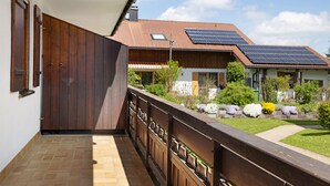 A balcony with a wooden railing, a tiled floor, and a view of a house with solar panels and a garden. - Apartment 'Haus Grüntensee' with Balcony and Wi-Fi (Wertach)