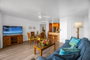 En stue med fjernsyn, spiseplads, køkken og en sofa.