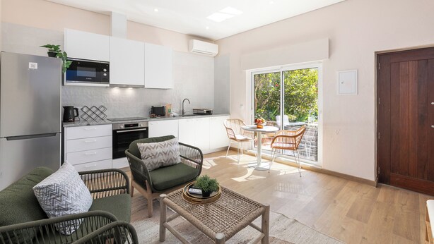 Eine moderne Küche mit weißen Schränken, einer eingebauten Mikrowelle und einer Kaffeemaschine. Es gibt eine Essecke mit Tisch und Stühlen sowie eine große Schiebeglasdoor zum Balkon.