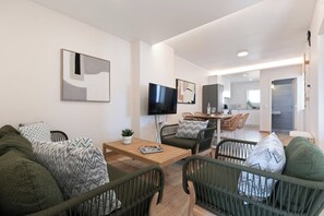 A modern living room with a sofa, chairs, a coffee table, a TV, and a dining area. - Atlântico Azul - Apartment E (Lagos)
