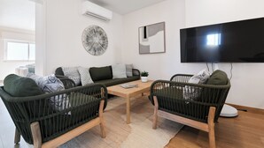 A modern living room with a sofa, two armchairs, a coffee table, and a flat-screen TV mounted on the wall. - Atlântico Azul - Apartment E (Lagos)