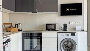 Uma cozinha compacta com micro-ondas, forno e máquina de lavar roupa, máquina de café e uma TV exibindo o logotipo do Google.