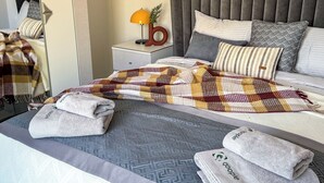 Uma cama bem arrumada com um cobertor xadrez, travesseiros e toalhas dobradas.