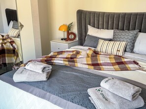 Ein ordentlich bezogenes Bett mit karierter Decke, Kissen und gefalteten Handtüchern.
