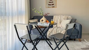 Quarto com sofá, uma mesinha com um vaso e um copo de suco de laranja, e uma cadeira.