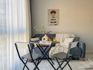 Ein Zimmer mit einer Couch, einem kleinen Tisch mit einer Vase und einem Glas Orangensaft sowie einem Sessel.