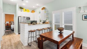 A modern kitchen with white cabinetry, a central island with bar stools, and a dining table. - Pet-Friendly Seacrest 4BR Beach Retreat+ Free Tickets: Dolphin Cruise & More! (Seacrest)