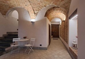 Ein Flur mit Treppe, weißen Stühlen, einem kleinen Tisch und einem Laternenleuchter.