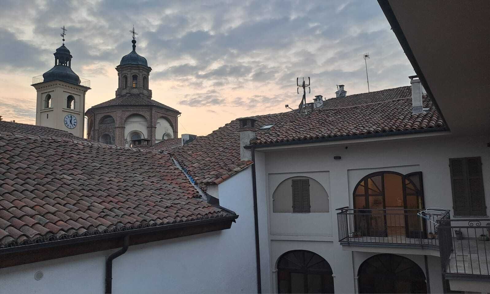 Un edificio con una torre de reloj y una campana, rodeado de otros edificios con tejados de tejas.