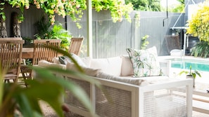 A patio area with a wicker sofa, dining table, chairs, and a view of a swimming pool. - West End Oasis with Pool and Entertaining (West End)