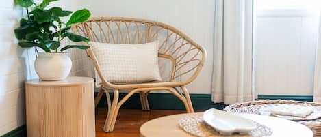 Ein Korbstuhl mit Kissen, ein Blumentopf, ein runder Holztisch und eine gewebte Tischmatte auf einem Tisch.