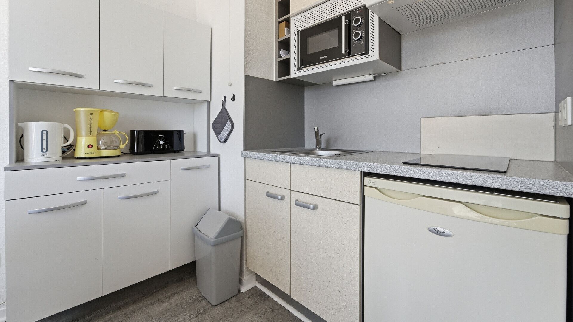Una kitchenette compacta con microondas, cafetera y tostadora.