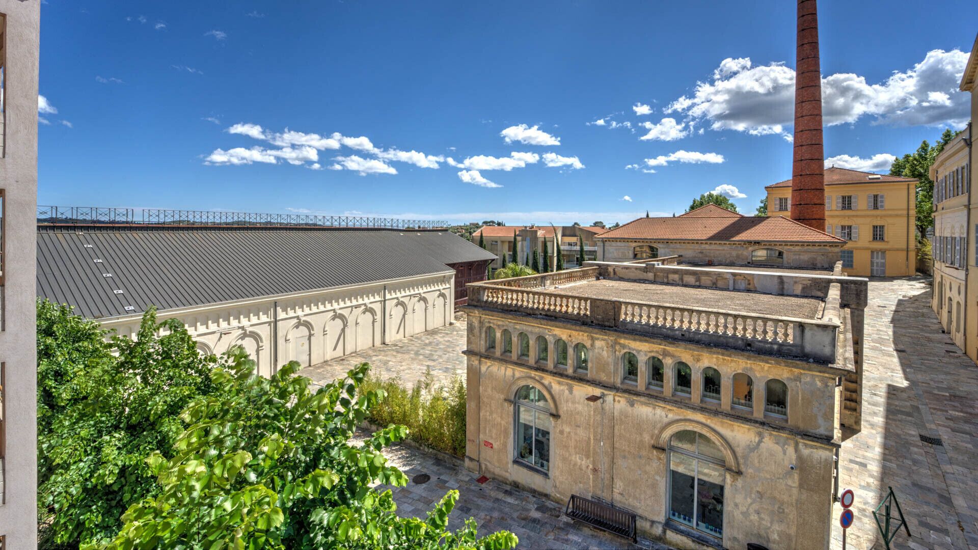A courtyard with historic buildings, a tall chimney, and a clear blue sky.