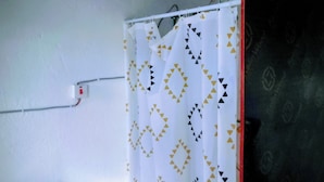 Een wit gordijn met een geometrisch patroon, een witte muur en een rood object aan de rechterkant.