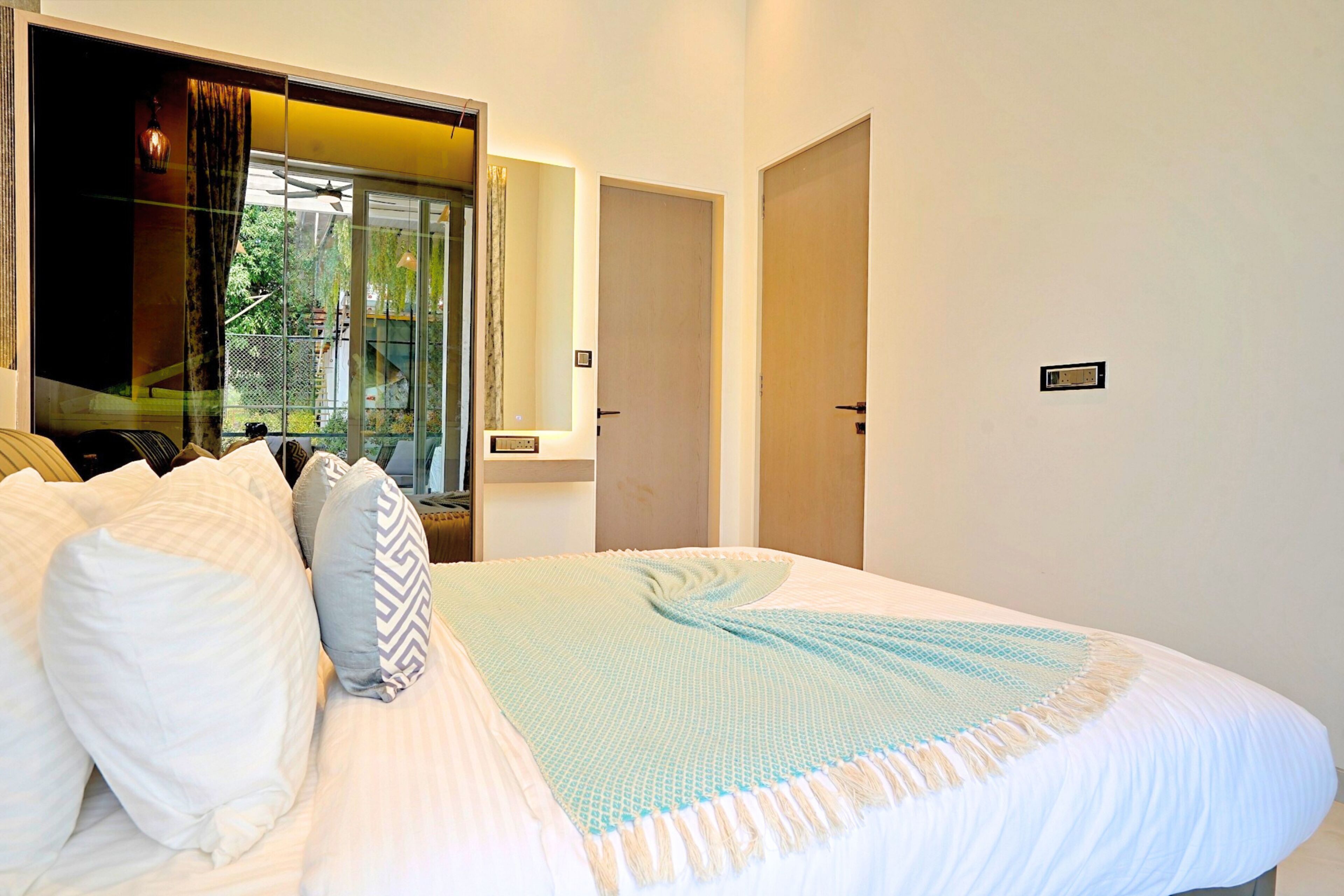 A bedroom with a large bed, a window with curtains, a door, and a small sign on the wall.