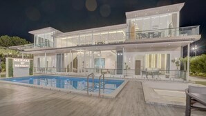 Une villa moderne à deux étages, dotée d’une piscine, de grandes baies vitrées et d’un espace extérieur bien éclairé.