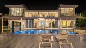 Une maison moderne à deux étages dotée d’une piscine, de deux chaises longues et d’une enseigne sur laquelle on peut lire : « MERAKI BY M9 VILLAS ».