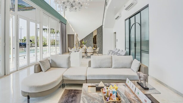 Un salon moderne avec un canapé d’angle, un lustre et de grandes fenêtres.