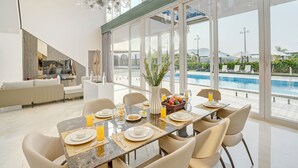 Un espace repas avec vue sur la piscine, un mobilier moderne et un lustre.