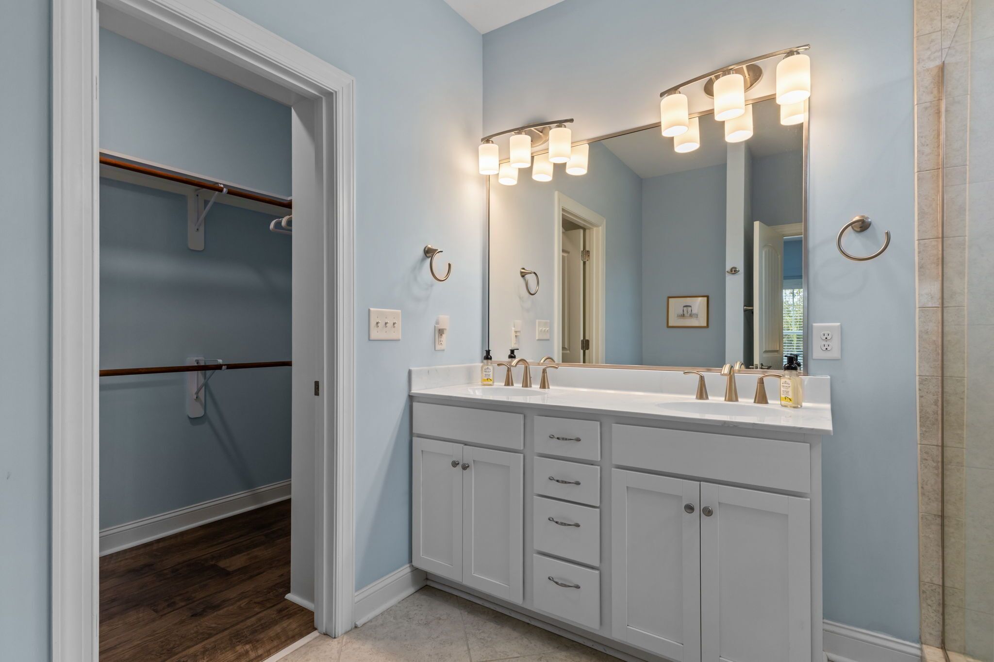 A bathroom with a double sink vanity, a large mirror, and a walk-in closet.