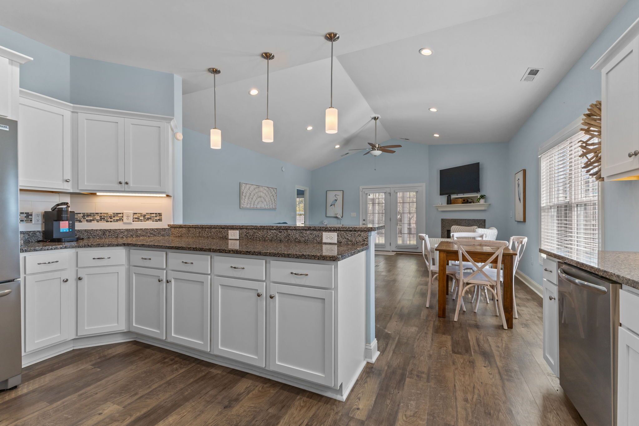A modern kitchen with white cabinets, granite countertops, and a dining area with a table and chairs.