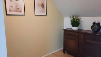 Un couloir avec deux tableaux encadrés accrochés au mur, une plante en pot, une horloge et un meuble en bois.