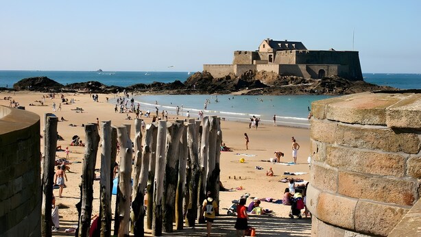 A beach with people, a castle-like structure, and a clear sky.