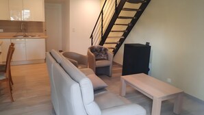 A living room with a sofa, a chair, a small table, a staircase, and a kitchen area.
