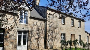 A stone building with multiple windows, a door, and a small garden area with grass and a few plants.
