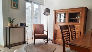 A dining area with a wooden table, chairs, a rug, a cabinet, a radio, and a potted plant.