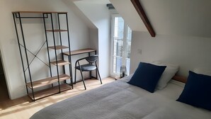 A bedroom with a bed, a desk, a chair, and a shelving unit.