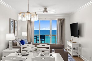 Ein modernes Wohnzimmer mit Essbereich, Fernseher und einem Balkon mit Meerblick.