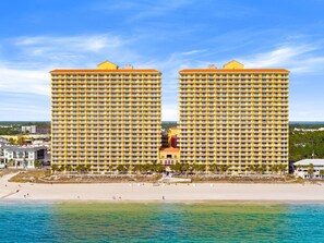 Ein Strandhotel mit zwei markanten, gelben Gebäuden, einem sandigen Strand und einem strahlend blauen Himmel.