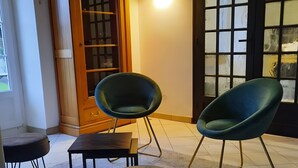 Een kamer met twee groene stoelen, een kleine tafel, een kast en een vloerkleed.